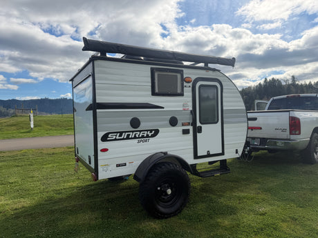This Sunray Sport rv rental, a compact travel trailer, is ready for adventure, hitched to a truck on a grassy site.