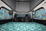 Cozy RV rental interior with a pop-top, patterned bed, colorful curtains, and fans for comfortable travel.
