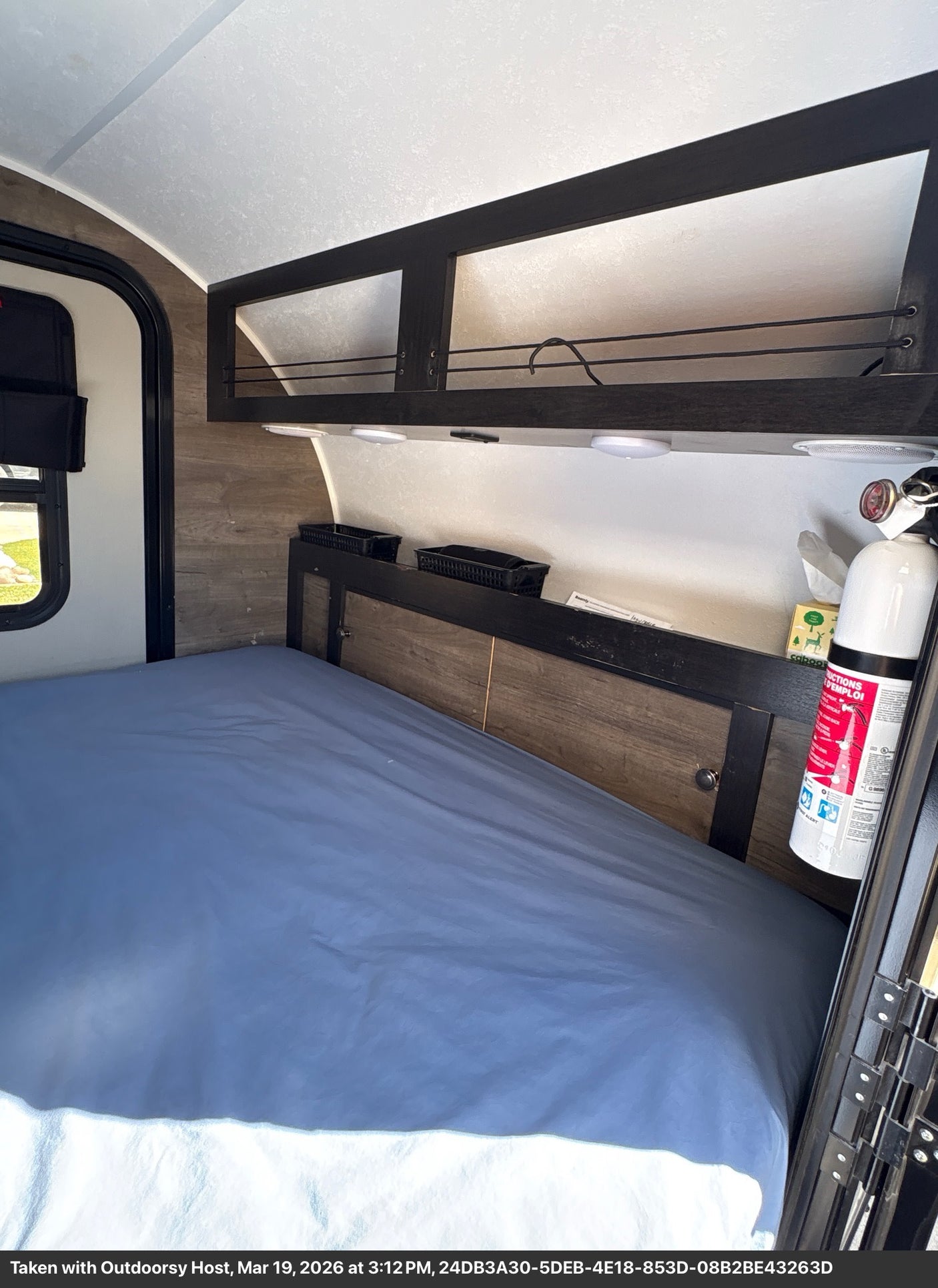 RV rental interior with a bed, overhead storage, and fire extinguisher for safety.