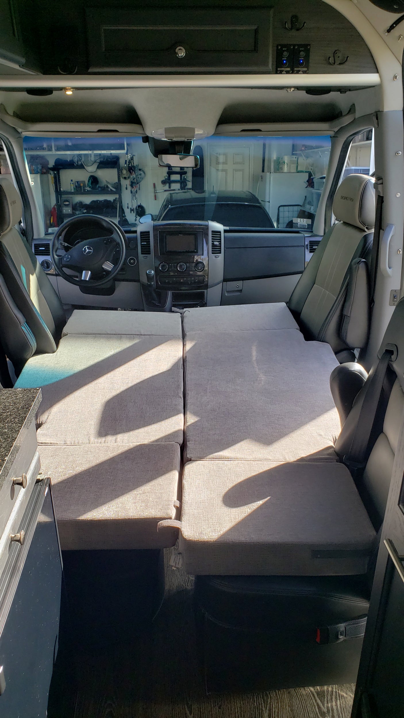 Spacious RV rental interior featuring a versatile bed/seating arrangement. View includes driver's area, kitchenette, and overhead storage.