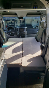 Spacious RV rental interior featuring a versatile bed/seating arrangement. View includes driver's area, kitchenette, and overhead storage.