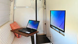 Inside an RV rental, a compact office with a laptop, monitor, and comfortable bench seating for remote work.