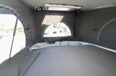 Inside an RV rental pop-top camper: a comfortable sleeping area with bed, canvas walls, and rear window.