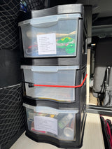 Inside an RV rental: stacked clear drawers neatly organize camping, first aid, and travel essentials with labels.