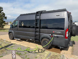 Dark grey rv rental camper van at a scenic campsite, hooked up with power and water, mountains in the distance.