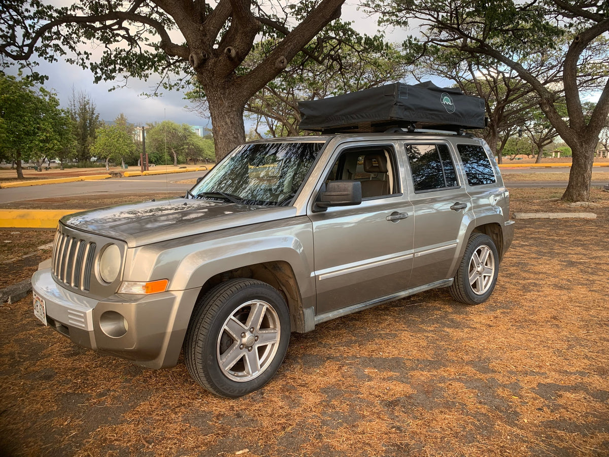 A light brown Jeep Patriot SUV with a rooftop tent, parked on dry ground under trees. Ideal for an RV rental outdoor trip. — photo 18