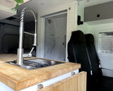 RV rental: Modern van conversion interior featuring a kitchen sink, shower, and rear passenger seats for comfortable travel.