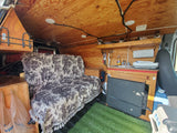 Cozy RV rental interior showing a kitchenette with a sink, wood paneling, a toile-patterned sofa, and storage.