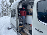 Cozy RV rental in a snowy forest. A person is inside the camper van, highlighting mobile winter living.