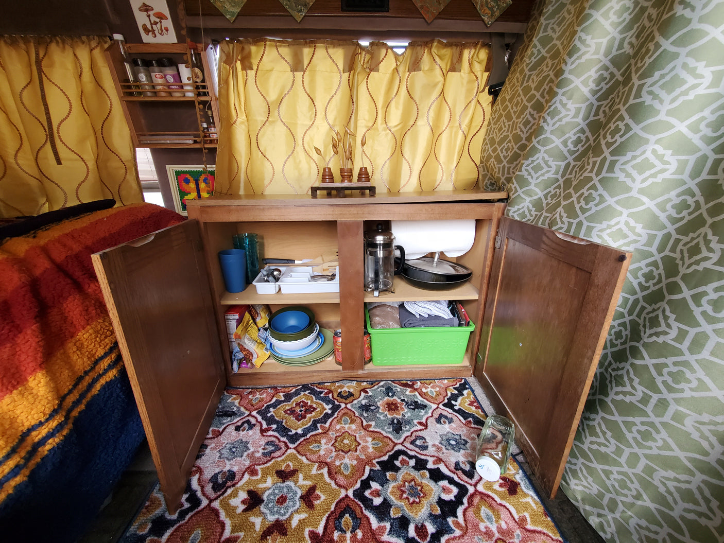 Cozy RV rental kitchen storage with open cabinet, revealing organized dishes, cooking tools, and a French press.