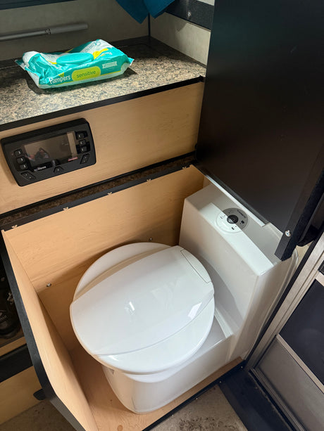 Compact RV rental bathroom with a Dometic toilet, Pampers wipes, and a REDARC control panel for comfort on the go.