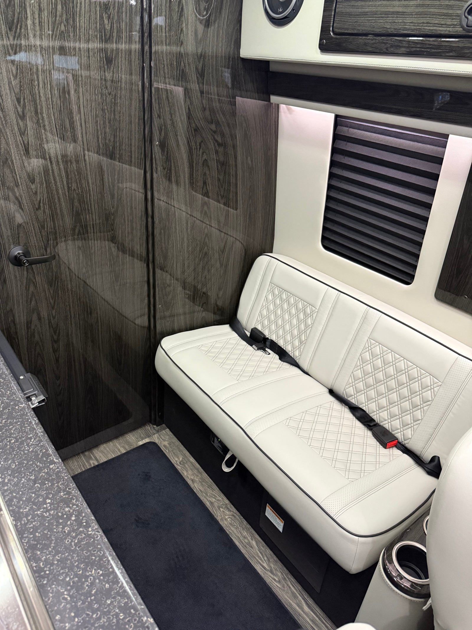 Step inside this RV rental: a pristine white bench seat contrasts with elegant dark wood paneling, ready for adventures.