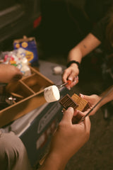 Enjoying s'mores by an RV rental! Hands hold marshmallows, Hershey's chocolate, and graham crackers for a sweet treat.