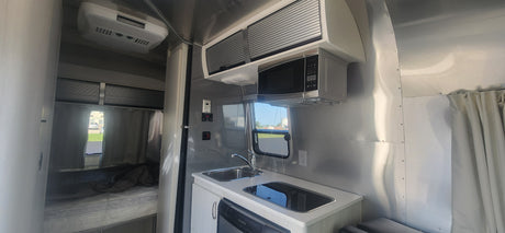 RV rental interior featuring a compact kitchen with microwave, sink, stove, and a cozy bedroom area.