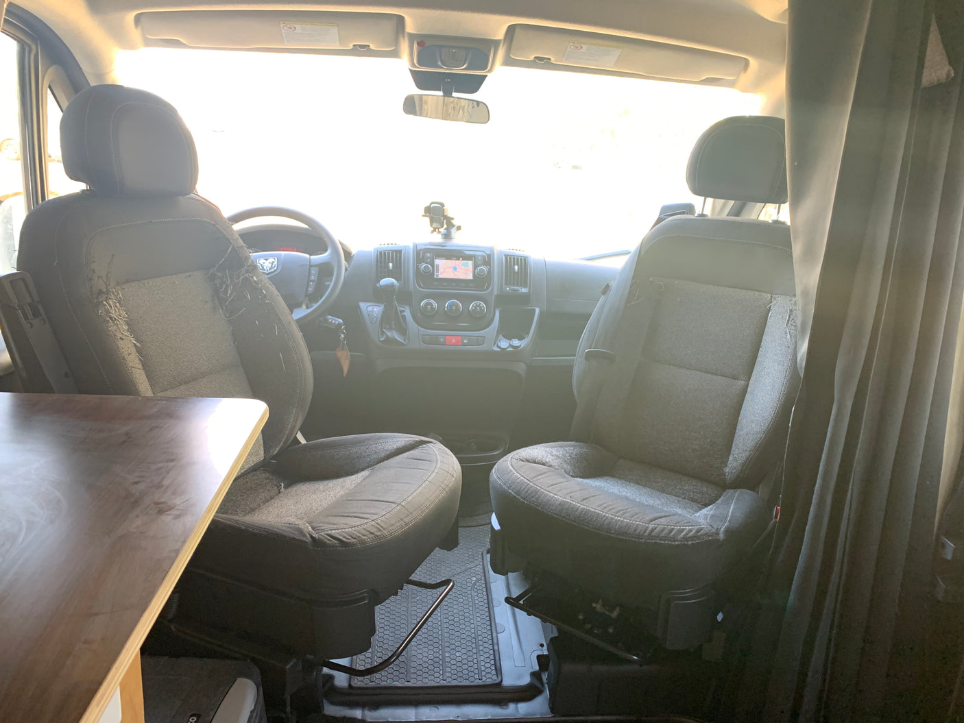 Interior of an RV rental van, showing front seats (one worn), dashboard, and a built-in table. Ready for travel.