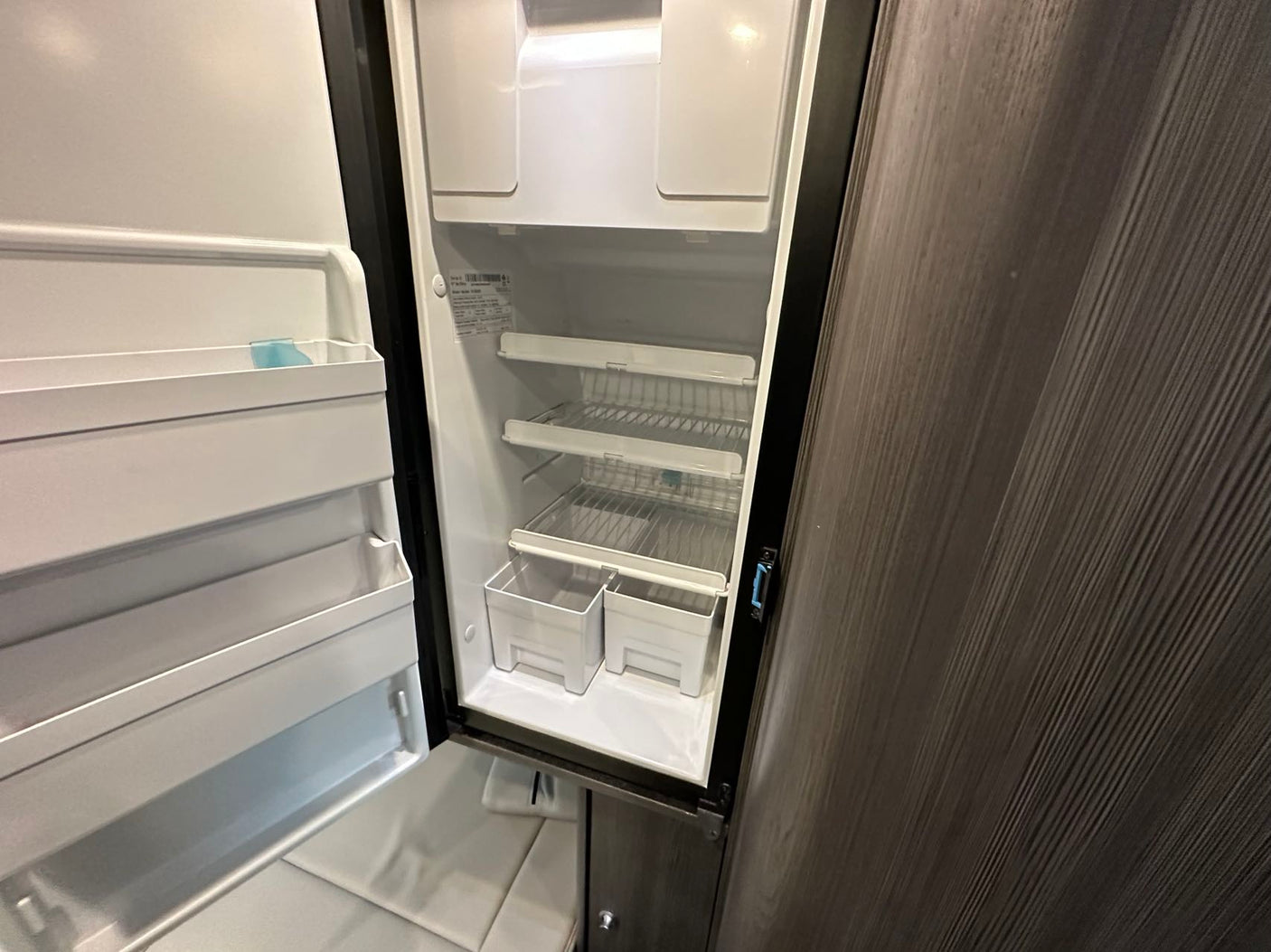 This empty rv rental refrigerator awaits your groceries. Featuring interior shelves, door storage, and crisper bins.