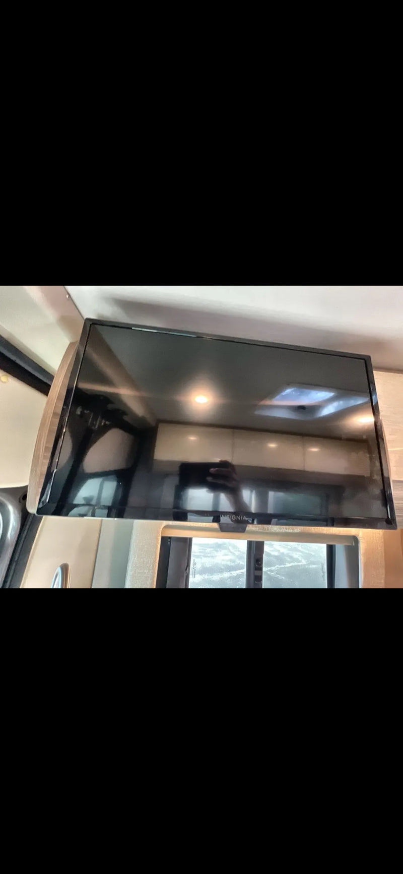 Inside an RV rental, a mounted Insignia TV for entertainment. The screen reflects the RV's interior and a window. — photo 7