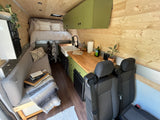 Cozy camper van RV rental interior features a kitchen, bed, and wood paneling. Ideal for travel and adventure.