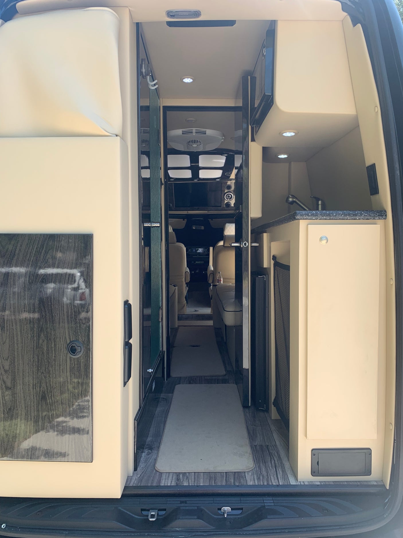 Step inside this luxurious RV rental. A modern camper van interior with kitchen, plush seating, and wide aisle viewed from the rear.