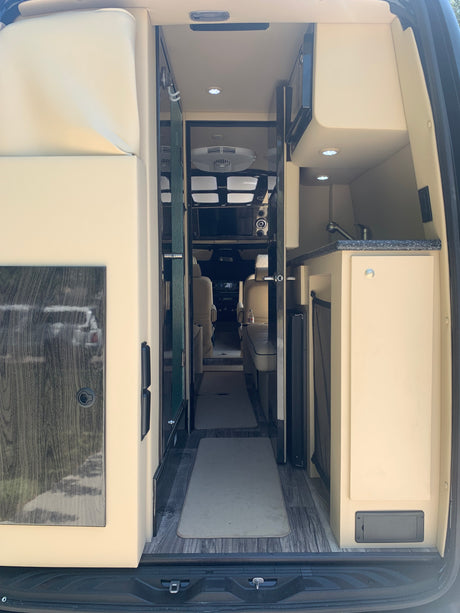 Step inside this luxurious RV rental. A modern camper van interior with kitchen, plush seating, and wide aisle viewed from the rear.