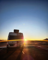 An RV rental parked, facing a vivid sunset over mountains. Epic road trip and travel views.