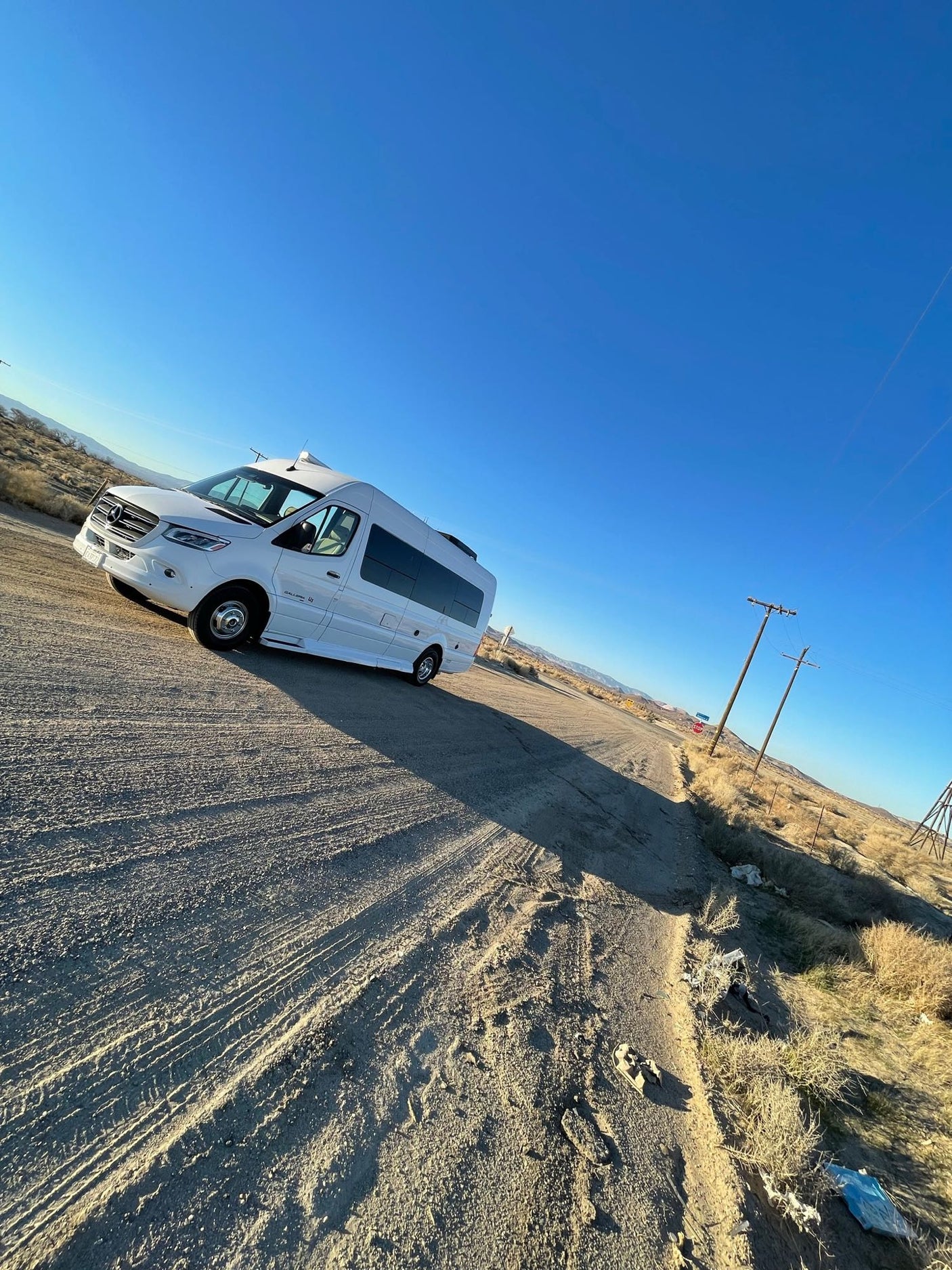 A white Mercedes-Benz Sprinter RV rental is parked on a dusty desert road under a clear blue sky.