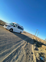 A white Mercedes-Benz Sprinter RV rental is parked on a dusty desert road under a clear blue sky.