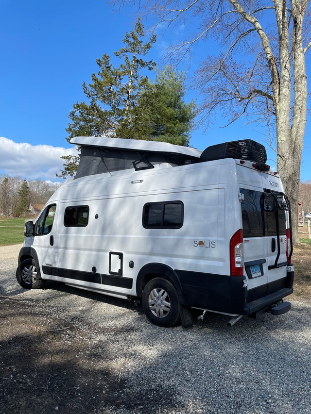 White Winnebago Solis camper van with pop-top extended, parked on gravel outdoors. Ideal for your next RV rental.