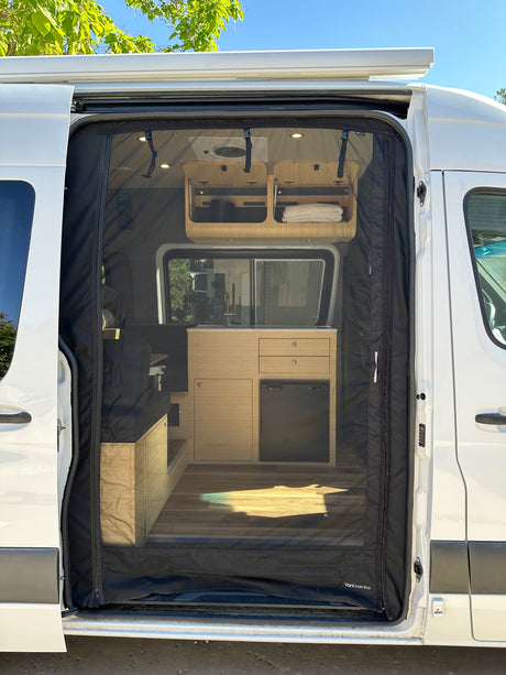 This RV rental features a camper van interior with a black mesh screen door, showcasing its kitchen, fridge, and living area.