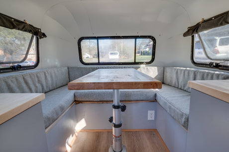 RV rental interior featuring a bright dinette with a wooden table, U-shaped benches, and multiple windows.