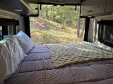 Cozy RV rental bed with a serene nature view through the screen window, perfect for camping relaxation.