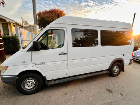 White Mercedes Sprinter 2500 camper van, perfect for an RV rental, parked street-side in golden hour light.