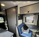 Experience comfort in this RV rental! Interior shows a compact living space with dinette, window view, and essential controls.
