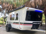 White Luna Rover teardrop camper RV rental with bike rack & awning, parked among palm trees.