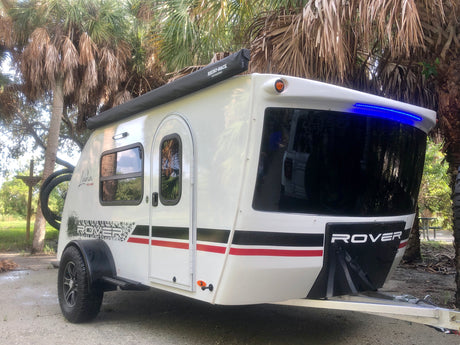White Luna Rover teardrop camper RV rental with bike rack & awning, parked among palm trees.