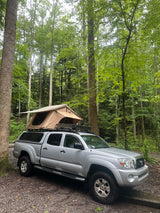 Overlanding adventure: Silver Tacoma truck with rooftop tent, a great alternative to an rv rental for forest camping.