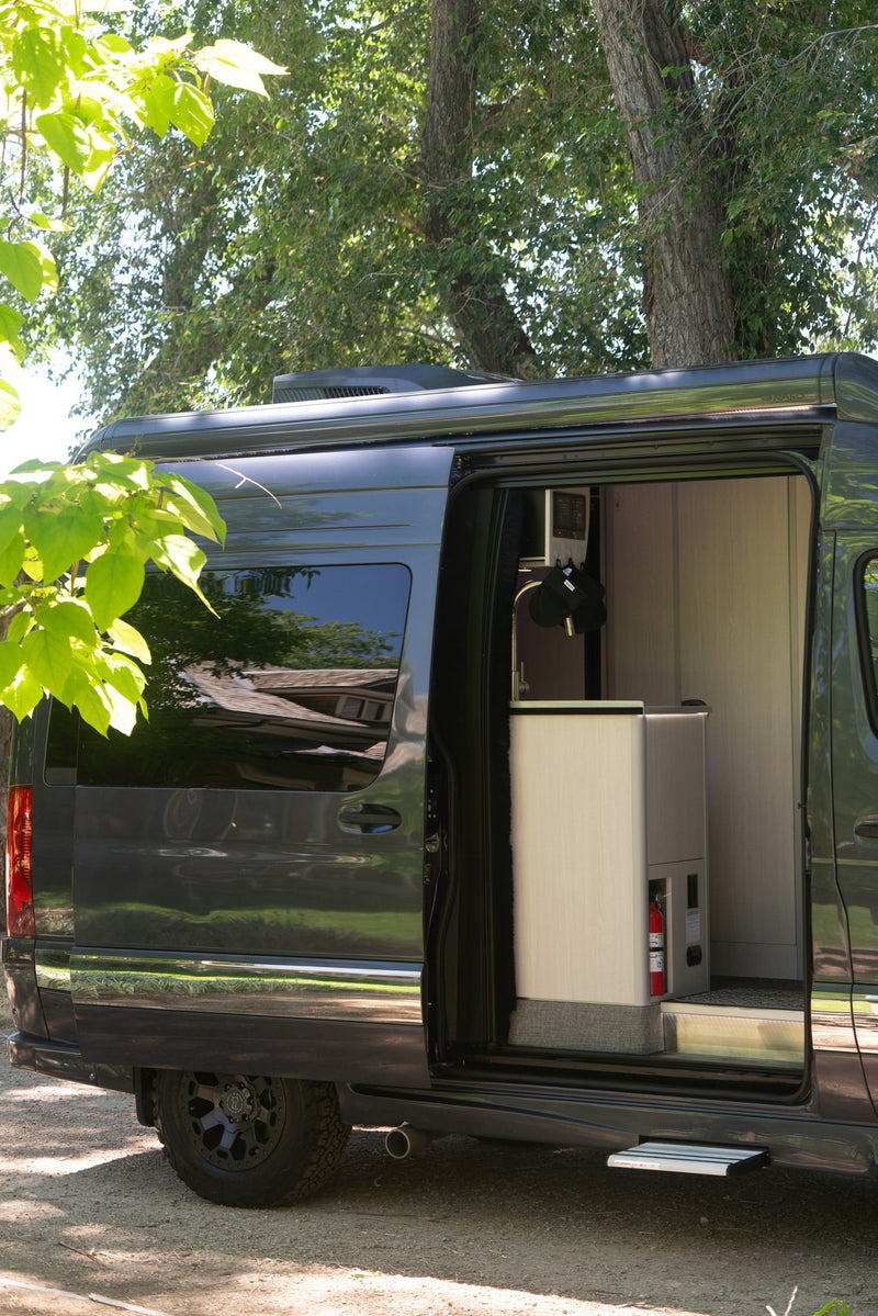 Dark grey RV rental with side door open, revealing a compact interior kitchen, fire extinguisher, and pull-out step, ready for adventure. — photo 7