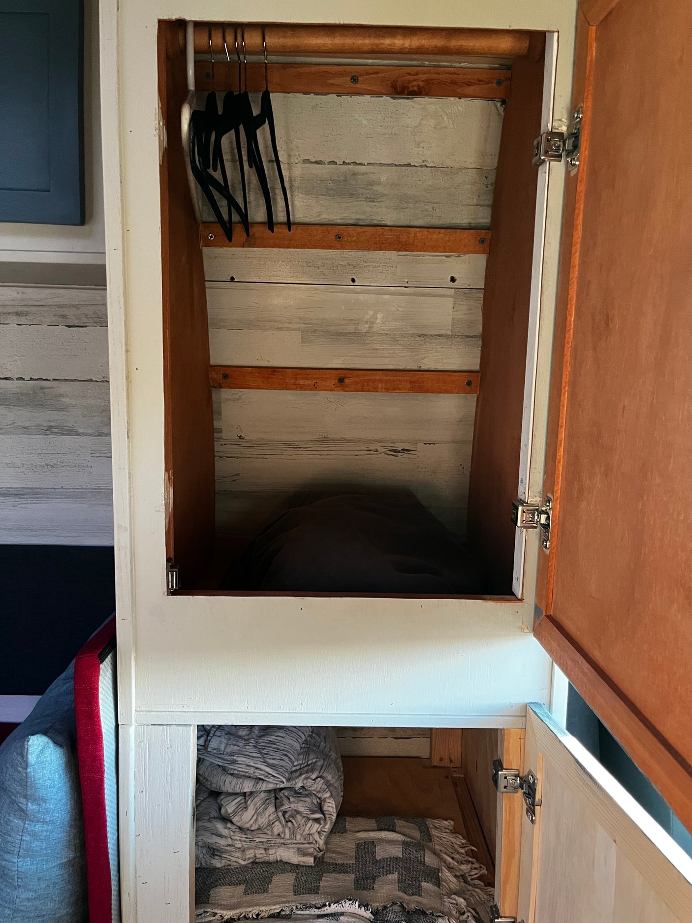 Inside an RV rental: a rustic closet with black hangers on a rod, wood plank walls, and neatly folded blankets below.