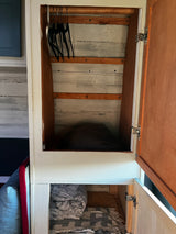 Inside an RV rental: a rustic closet with black hangers on a rod, wood plank walls, and neatly folded blankets below.