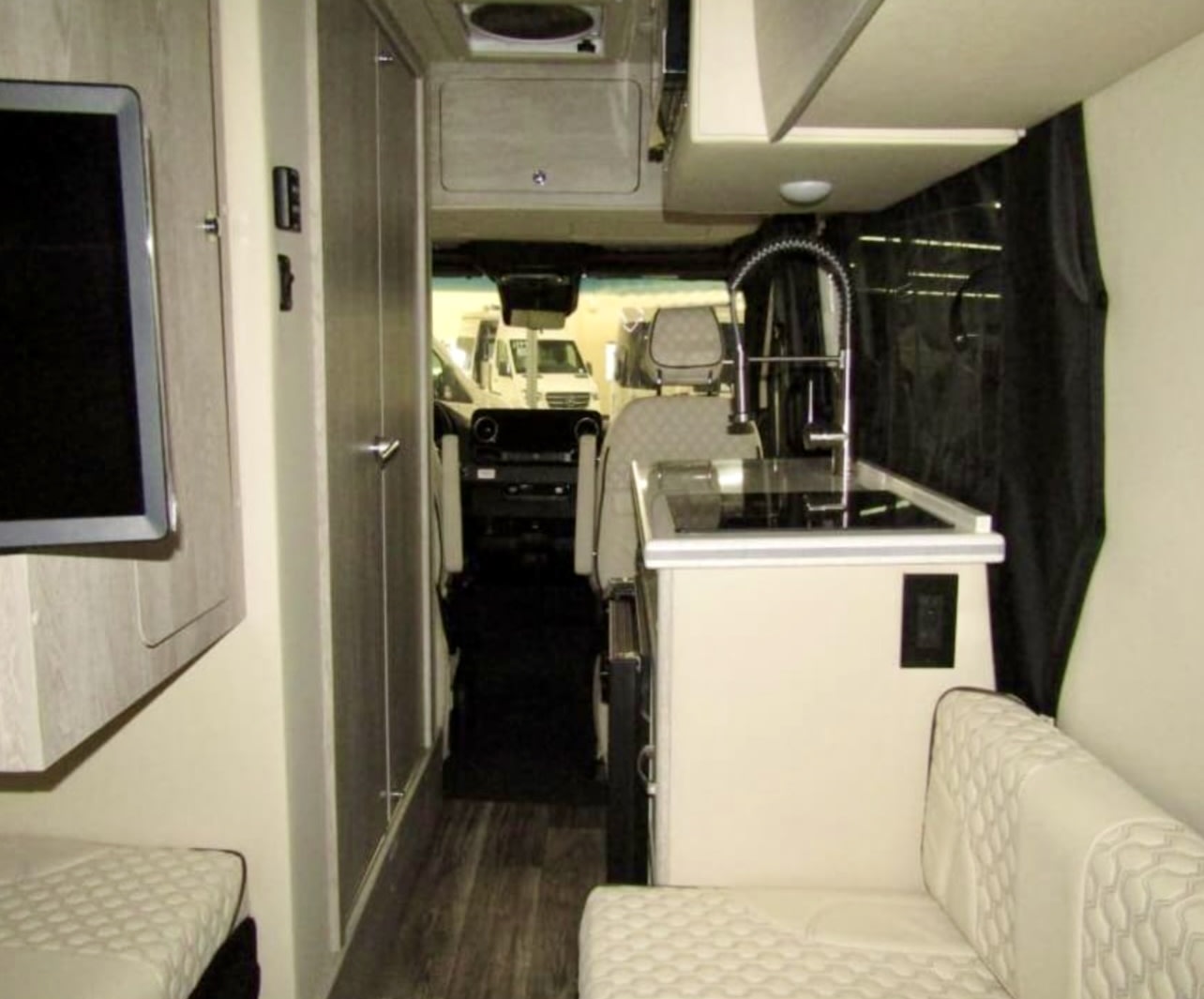 View inside a modern RV rental. Features include a galley kitchen, comfy seating, TV, and front cabin view. — photo 4