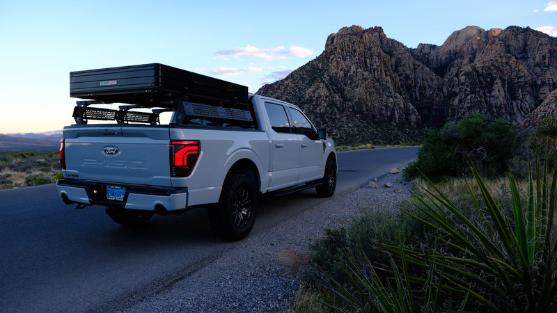 This Ford F-150 pickup with a rooftop tent, ideal for an RV rental, is parked on a desert road with rugged mountains. — photo 17