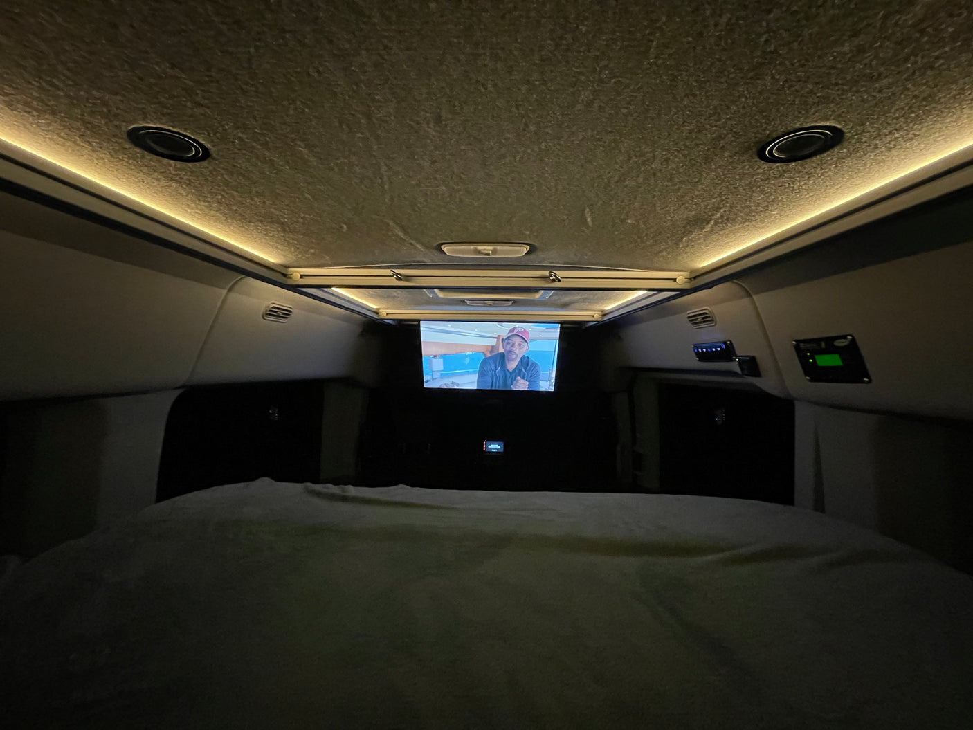 Cozy RV rental sleeping area at night, featuring a TV screen, ambient ceiling lights, and control panels.