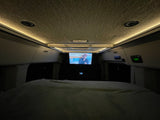 Cozy RV rental sleeping area at night, featuring a TV screen, ambient ceiling lights, and control panels.