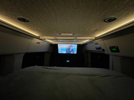 Cozy RV rental sleeping area at night, featuring a TV screen, ambient ceiling lights, and control panels.