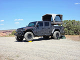 Dark gray Jeep Gladiator with rooftop tent deployed, ready for an RV rental adventure in the arid landscape.