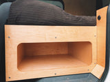 RV rental van conversion with custom wooden bed frame, open storage cubby, and power outlet.
