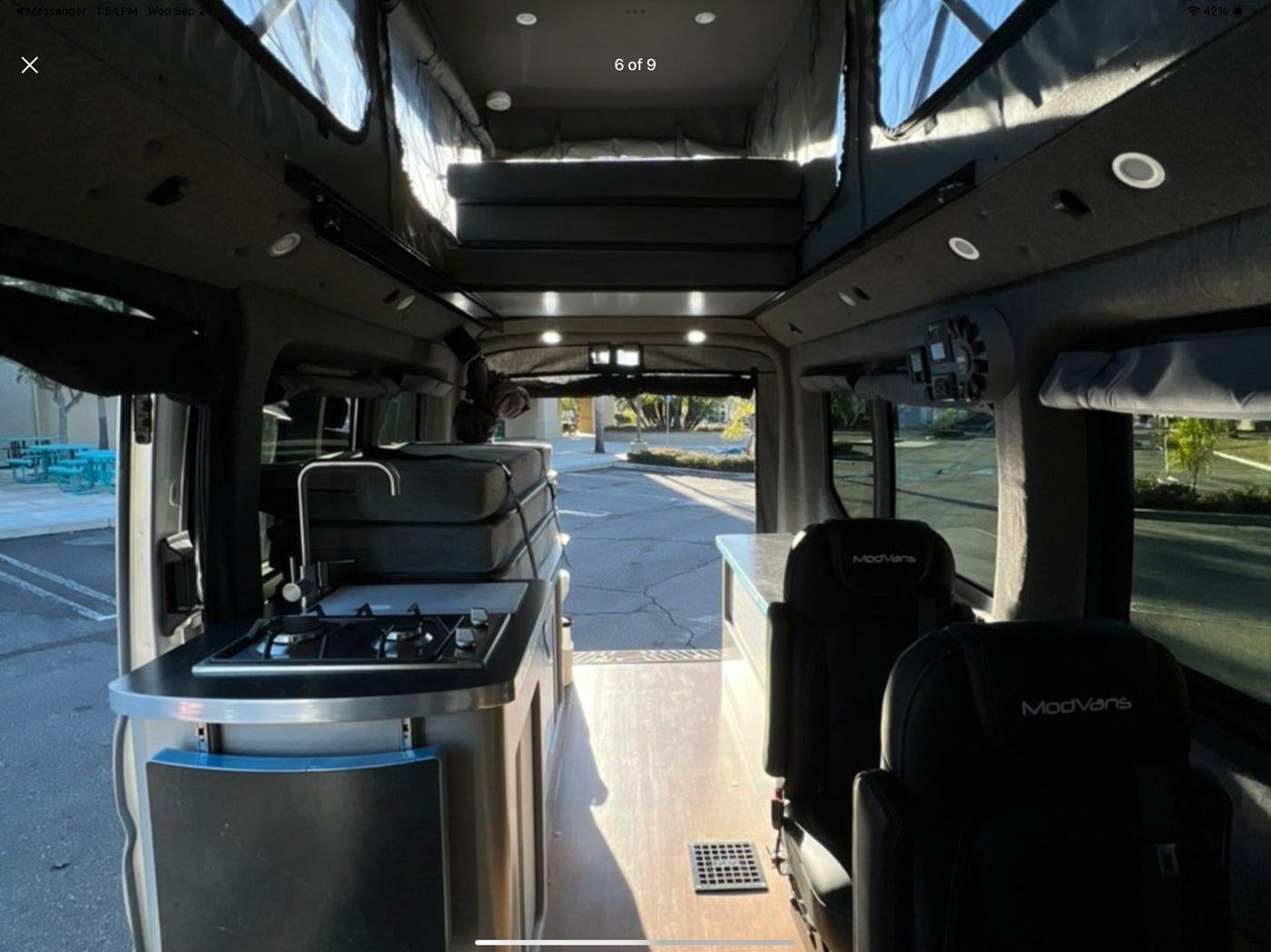 Explore this ModVans rv rental: a cozy camper van interior with a kitchenette, elevated bed, and comfortable rear seating. — photo 2