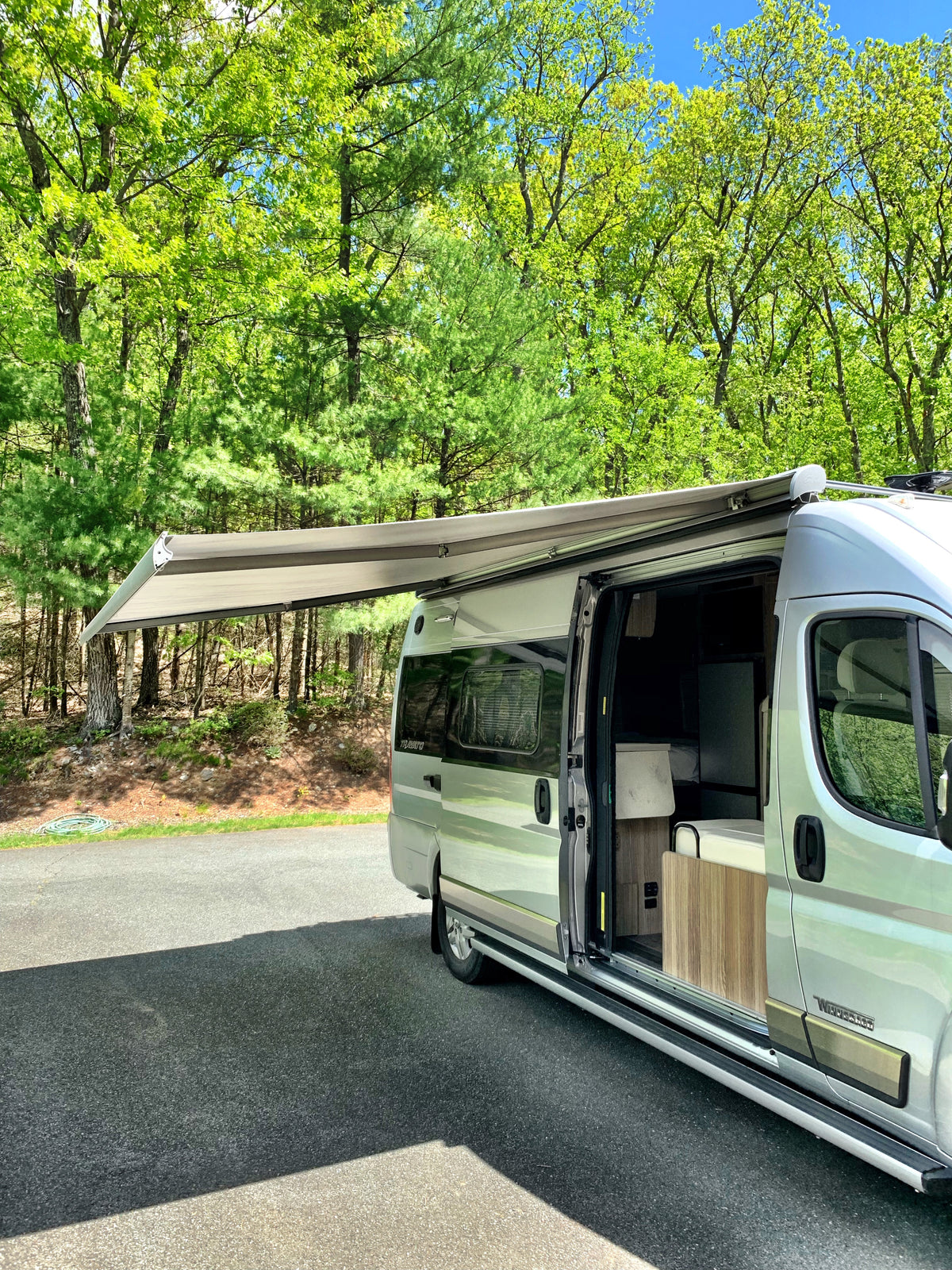 An RV rental camper van is parked with its awning extended and door open, surrounded by lush green trees on a sunny day. — photo 14
