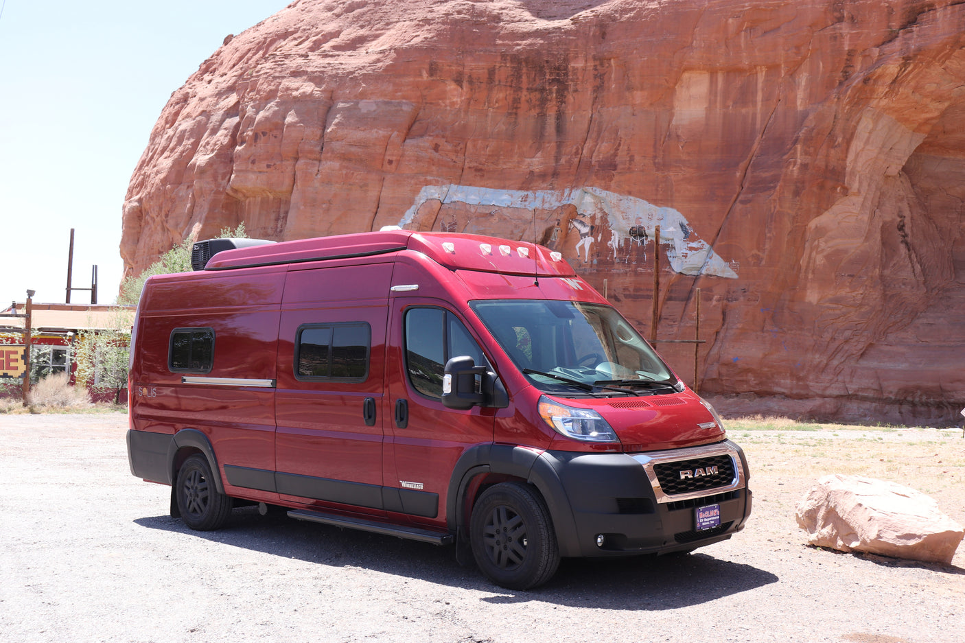 Red RV rental van by a scenic red rock cliff adorned with a large mural. Your next adventure awaits!