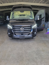 Sleek black Mercedes-Benz Sprinter van for RV rental, headlights on, driver's door open, parked indoors.